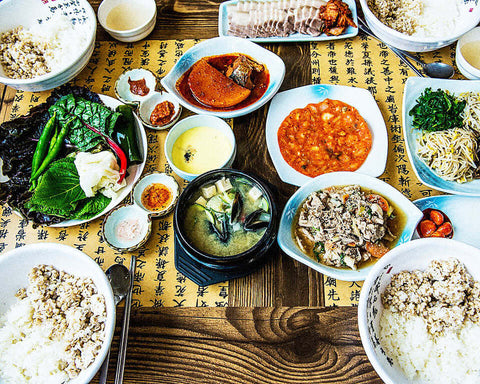 A spread of Korean food dishese including rice, kimchi, banchan, vegetables, on a restaurant table; natural wine, primal wine - primalwine.com