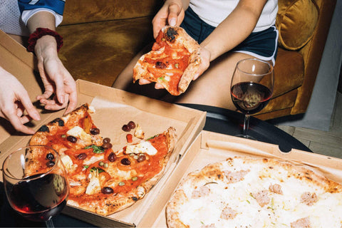 Two people eating pizza from pizza cartons and drinking natural wine, primal wine - primalwine.com