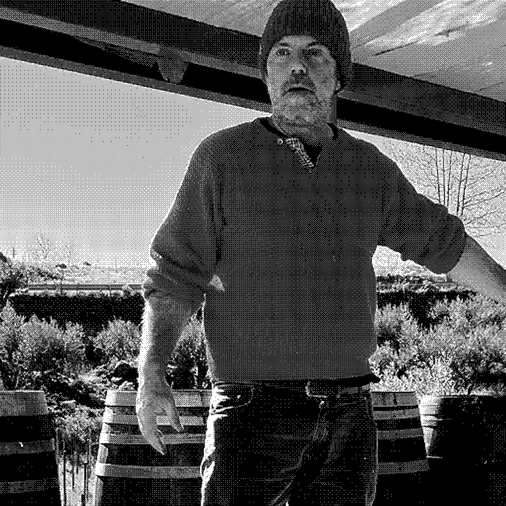 Davide Bentivegna, natural wine producer of Etnella, standing among barrels with Mount Etna behind his vineyard in Sicily, Italy