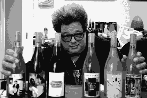 Scott Sampler leaning over a table with six bottles of his Scotty Boy and CCGP wines, wearing glasses and a printed t-shirt