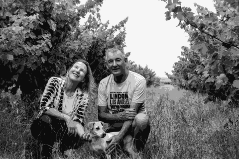 Suzi Hilder and Wayne Ahrens crouching in their Vine Vale vineyard with their dog