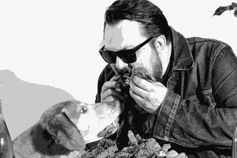 Andy Young of St. Reginald Parish sharing fried chicken with his dog, surrounded by bottles of The Marigny wines