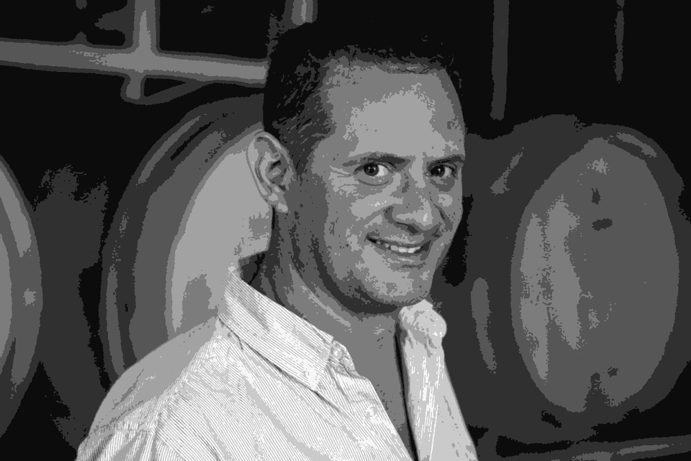 Gustavo Bauzá, head enologist at Casa de Uco, smiling in the winery barrel cellar holding a glass of wine