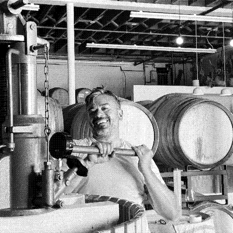 Jason Charles, natural wine producer of Vinca Minor, smiling beside his basket press in his California cellar